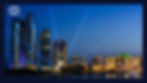 UAE night time cityscape with illuminated skyscrapers and buildings. Blue beams of light, clear sky, and water reflecting lights.