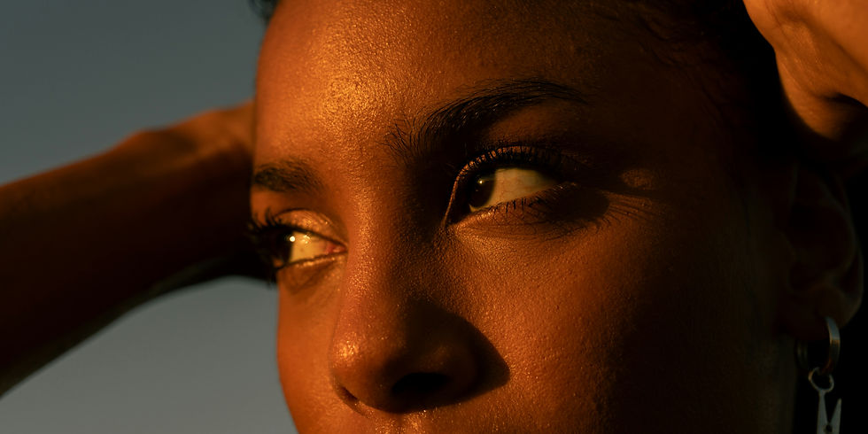 Close-up portrait of a thoughtful woman in warm sunset light, highlighting her expressive eyes and natural skin texture.