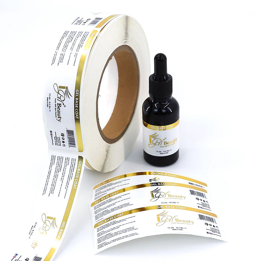 Un flacon avec pipette pour cosmétiques sur lequel on a apposé une étiquette personnalisée blanche et dorée. Devant on peut voir 3 étiquettes posées à plat et le rouleau de ces mêmes etiquettes à gauche