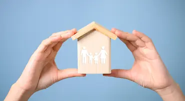wooden-house-protected-by-hands-on-blue-background-2026-01-09-12-34-54-utc copia.webp