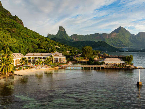 Tropical resort on a calm lagoon with palm trees, and green mountains under a partly cloudy sky. Cook's Bay Hotel in Moorea, French Polynesia.