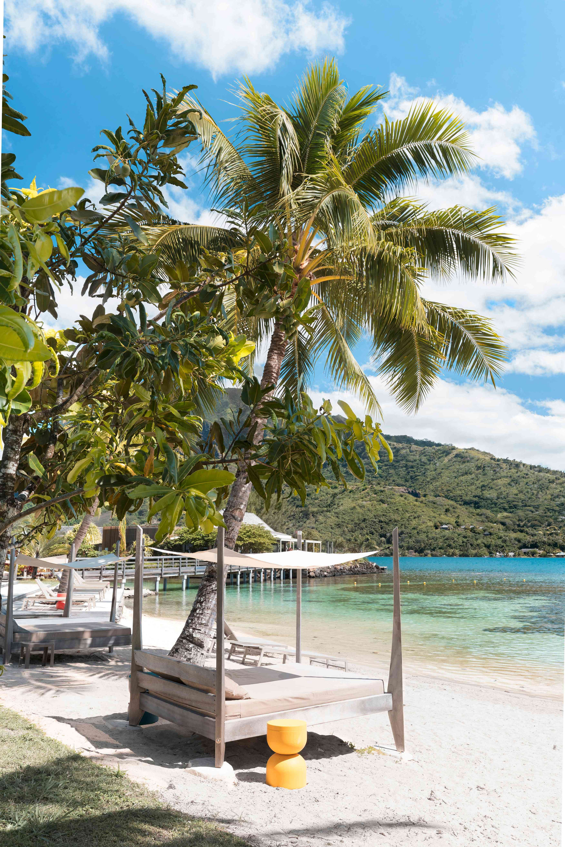 Sunbeds and loungers on a white beach sand with crystal clear water in the background, in Moorea.