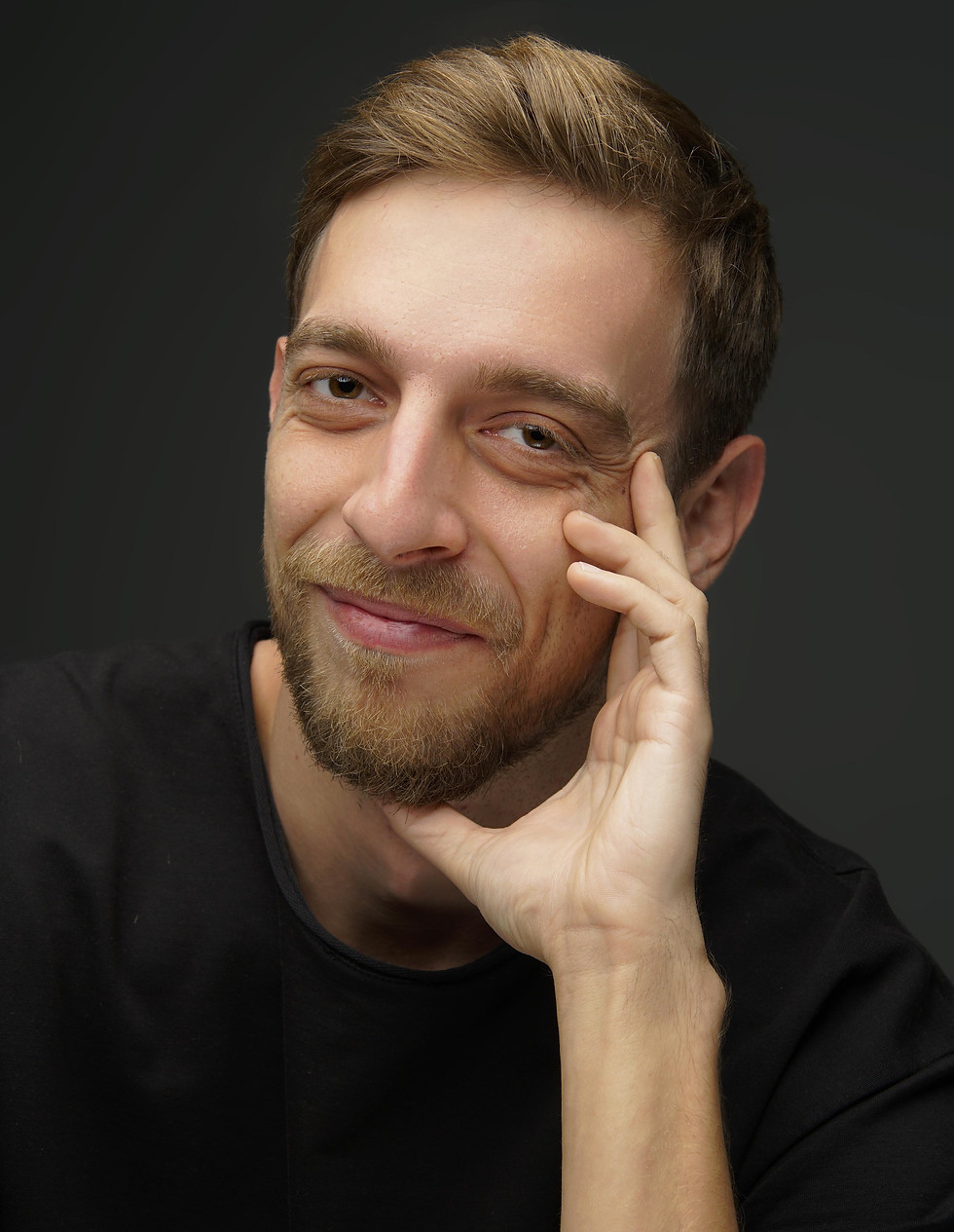 Smiling man in black t-shirt, posing with hand on face. uptownentertainment