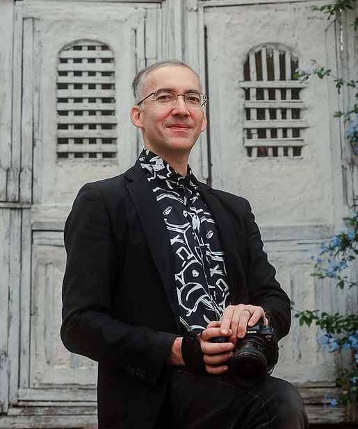 Giuseppe Marino Titolare di Foto bnb (B&B), Uomo sorridente in giacca nera con fotocamera, in piedi davanti porte bianche.