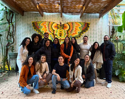 Grupo de 16 pessoas posando sorrindo em um jardim com a imagem de uma borboleta ao fundo.