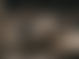 Interior designer in gray suit using two phones for social media in stylish furniture store with beige sofas and warm lighting. Modern decor creates an inviting ambiance.