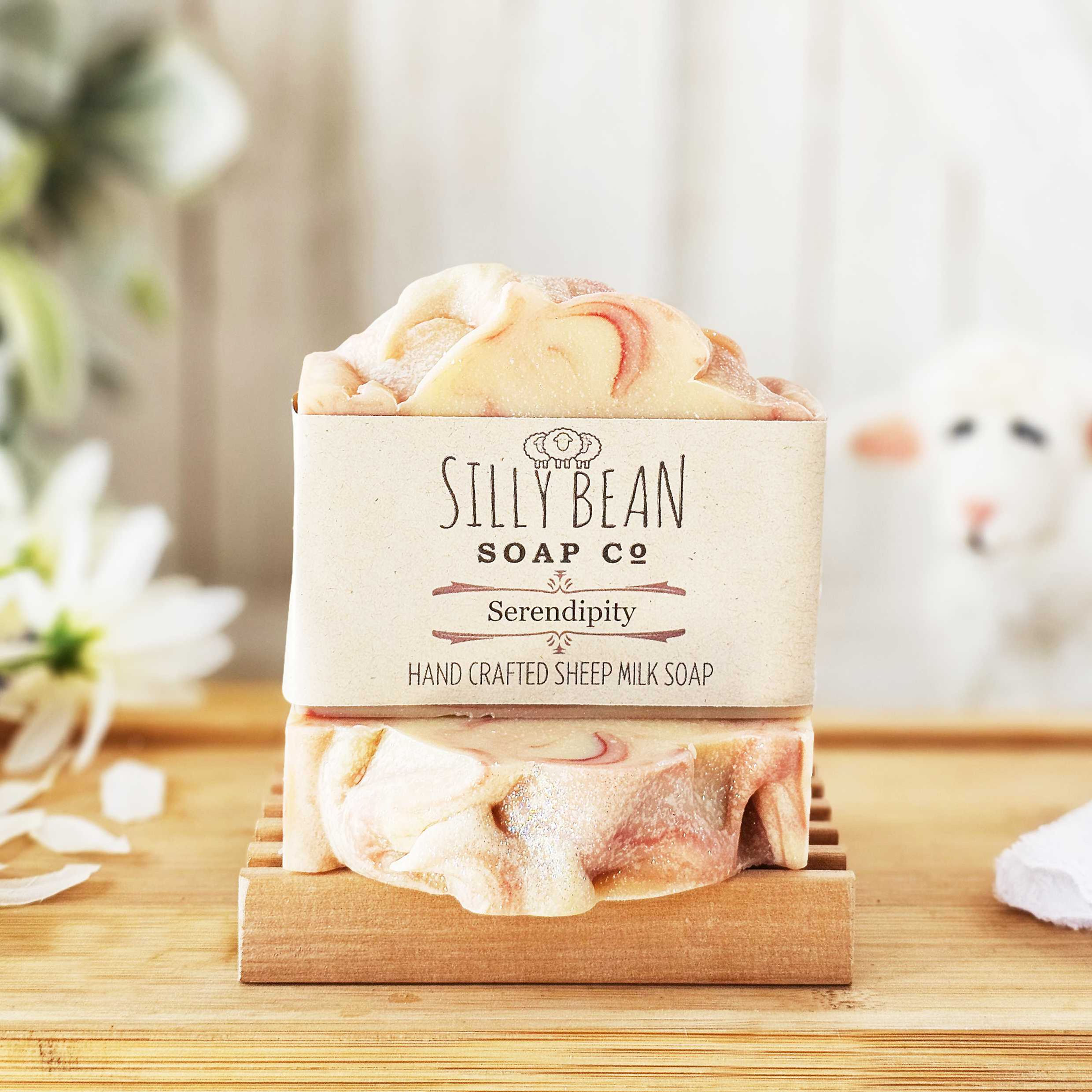 Labeled bar of soap sitting on top of one laying flat. Flower petals to the left and a sheep to the right.