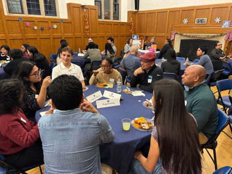 Groups of students and alums sitting, eating, and talking at round tables.