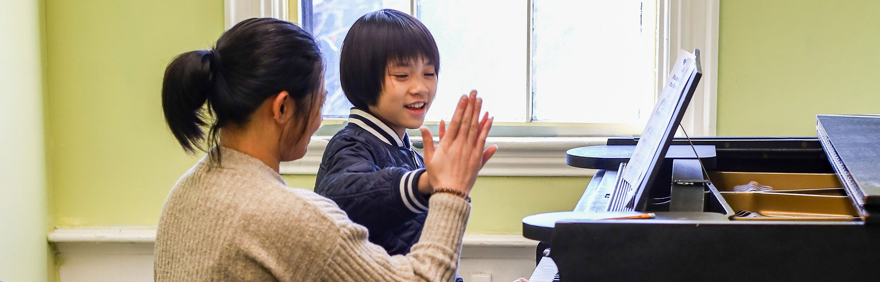 Happy child high-fiving teacher during a piano lesson in Cambridge, Massachusetts