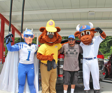 Four people posing together, including Sam The Bear, at Sam's Xpress Car Wash