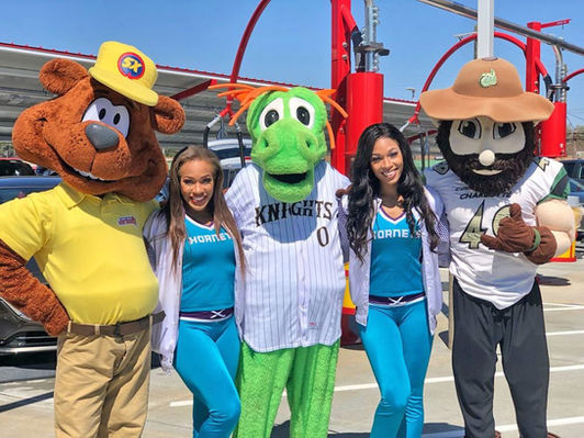Group photo of mascots and cheerleaders smiling at Sam's Xpress Car Wash