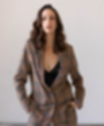 A female model wearing a brown suit standing in front of a white backdrop.