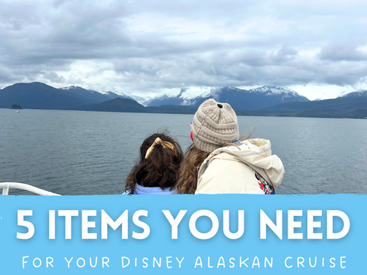 A bundled-up adult and child stand at the railing of a Disney Alaska cruise ship, facing snow-covered mountains and icy waters under a cloudy sky. Text overlay reads “5 Items You Need for Your Disney Alaskan Cruise” in bold white and blue lettering, promoting essential cruise packing tips.
