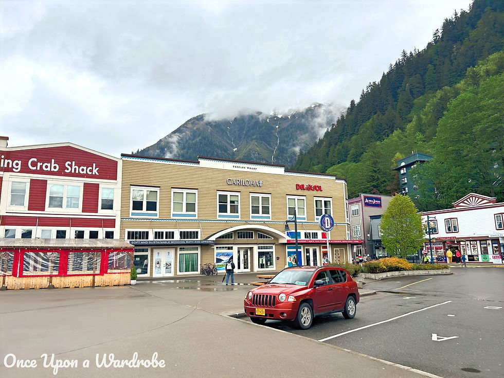 Colorful storefronts and shops in downtown Juneau, Alaska, with mountains and clouds in the background.