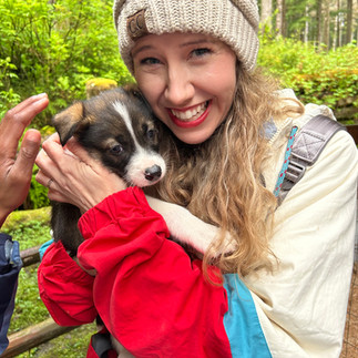 Ashlie smiling and holding an adorable husky puppy at a sled dog camp in Juneau, Alaska.