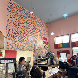 Bright and colorful interior of a Jellyfish Donuts with rainbow dot wall mural and customers ordering drinks.