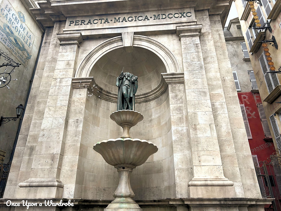 Stone fountain with a wizard statue inside The Wizarding World of Harry Potter – Ministry of Magic at Epic Universe, framed by an arched stone alcove with engraved magical text.