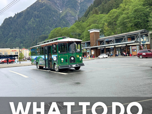 Green Juneau Trolley driving through the port area of Juneau, Alaska, with misty mountains in the background, promoting things to do on a Disney Alaska Cruise.