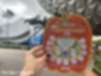 A guest holds a Pluto’s Pumpkin Pursuit 2025 scavenger hunt map in front of Spaceship Earth at Epcot during the Halloween season.