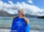 Ashlie standing in front of a glacial lake and snowcapped mountains in Alaska, wearing a blue “Golly What a Day” Disney Cruise sweatshirt and a cozy knit beanie — the perfect layered outfit for a chilly port day on a Disney Alaska Cruise.