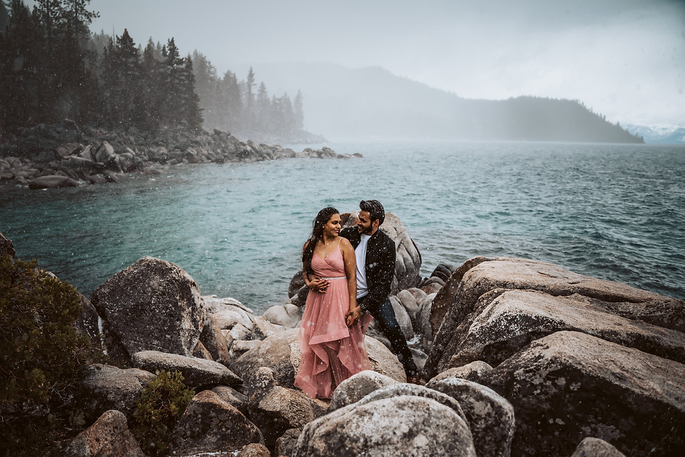 A couple standing on the boulders of Lake Tahoe and getting snowed on