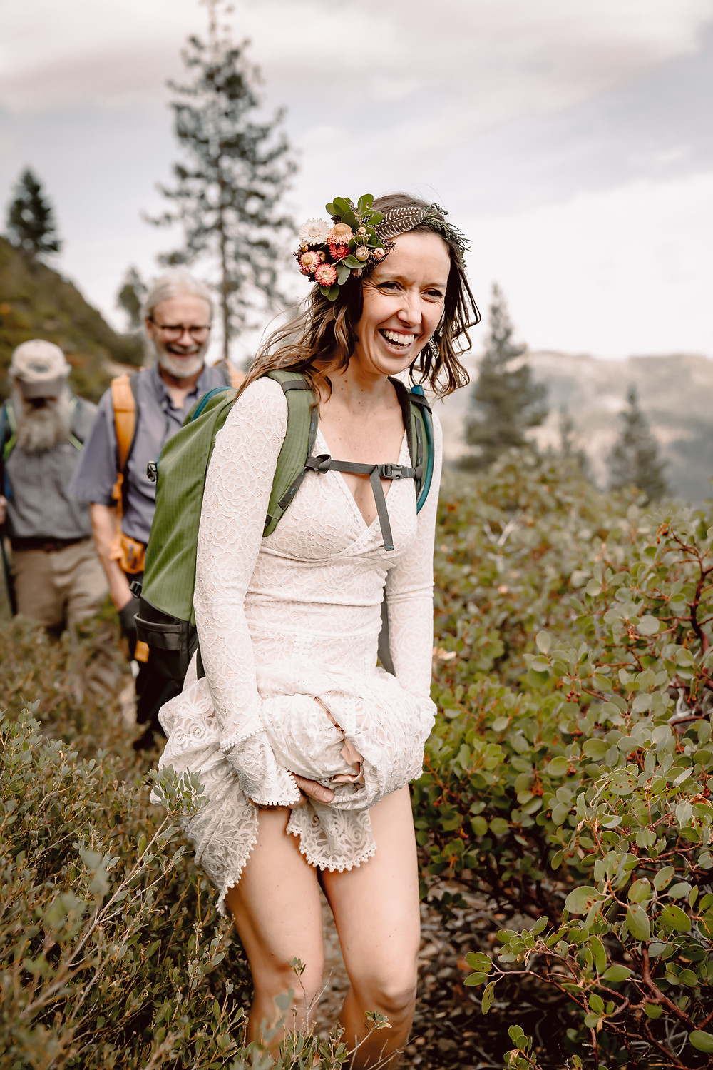 An adventure elopement bride hiking in a long sleeve lace dress and holding it up so it doesn't get snagged