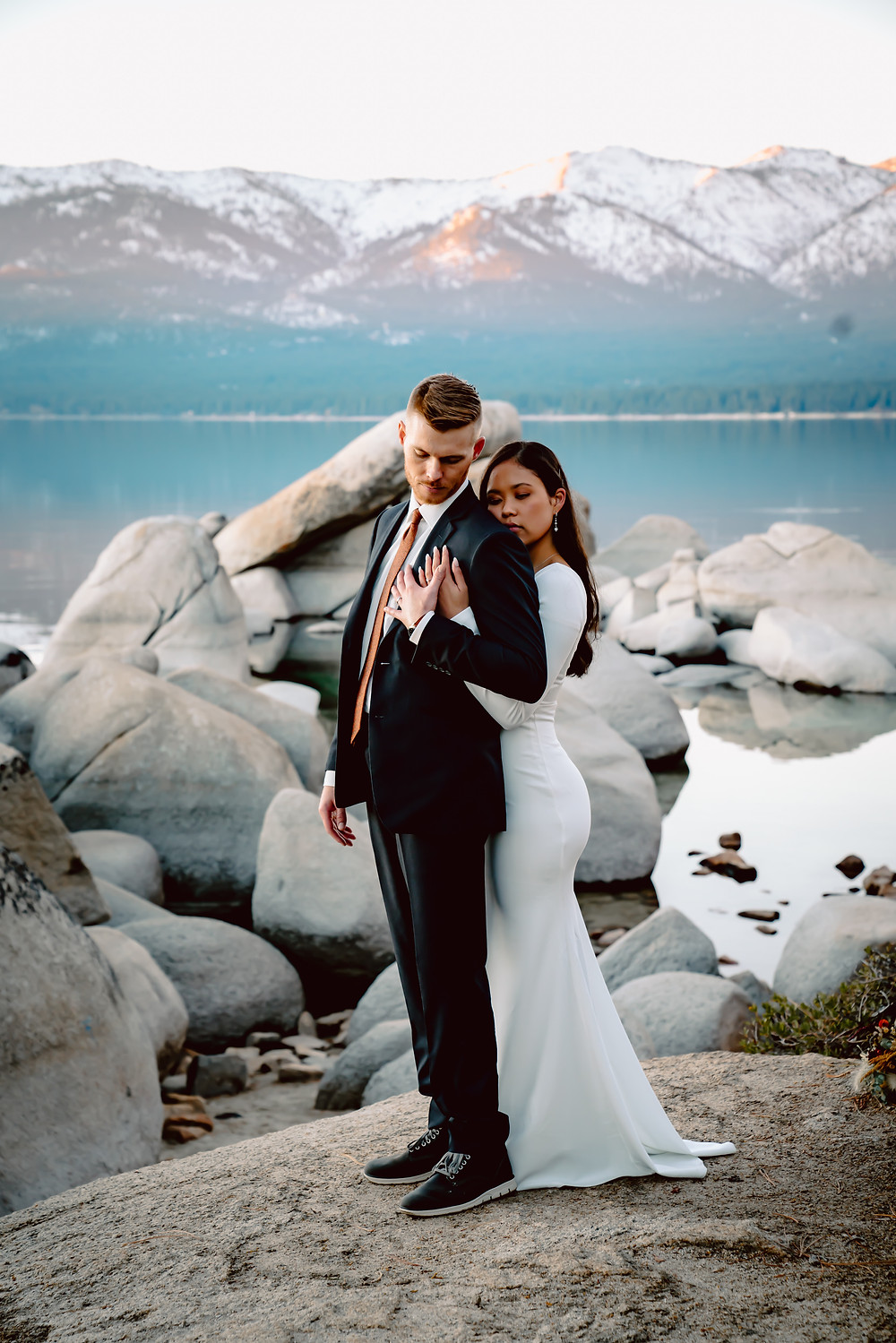 An elopement bride in a long sleeve dress hugging her new husband in front of the mountains of Lake Tahoe