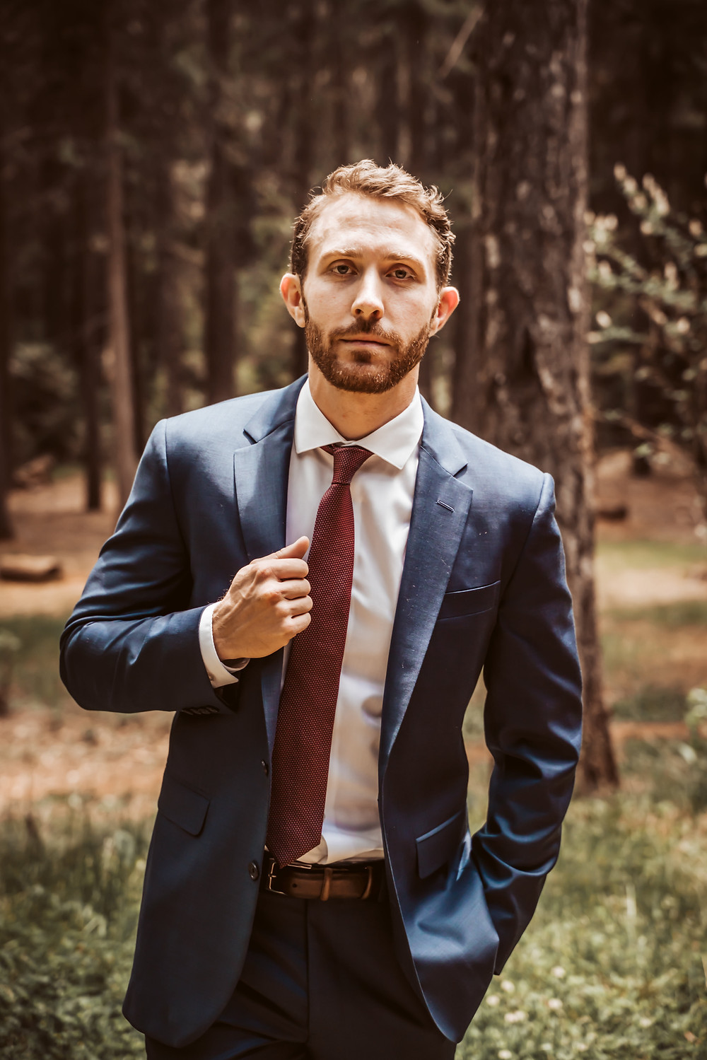 A groom wearing a navy blue suit with red tie and easy slacks on his wedding day