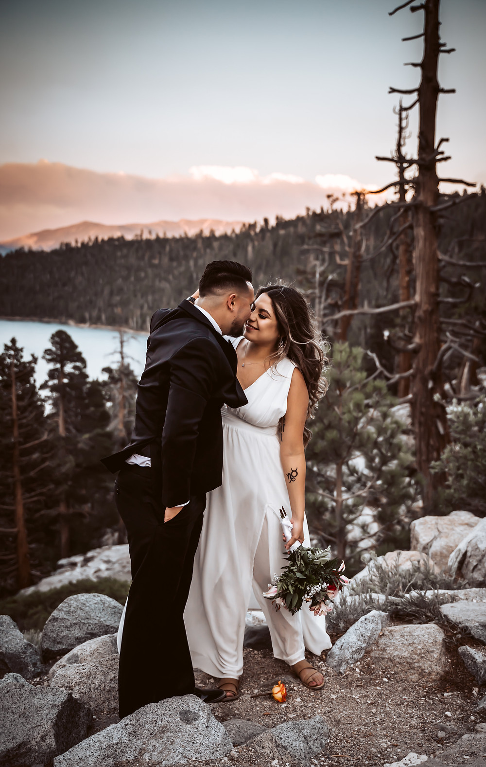 A elopement couple kissing and standing on a giant boulder in Emerald Bay in Tahoe with the Tamarack fire behind them