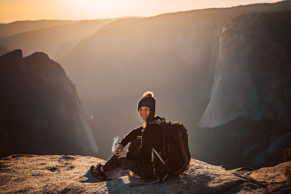 A elopement photographer wearing a hiking backpack sitting on a rock overlooking the sunset on the top of Yosemite Valley