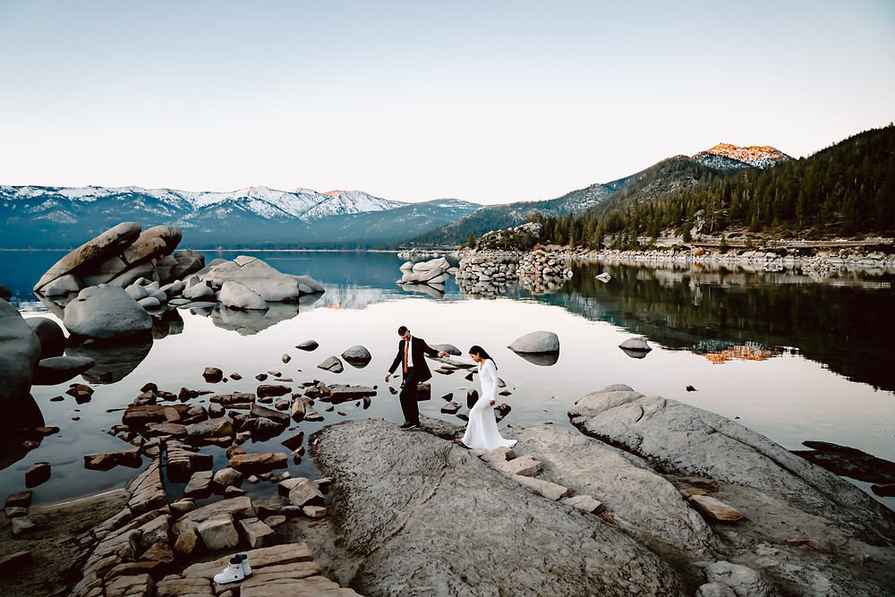 An elopement couple walking on rocks in Tahoe with the snowy mountains in the backdrop