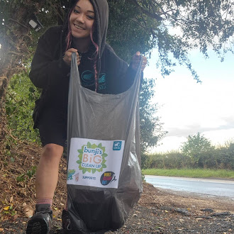 Woman holduing a bin bag. The background has a river to the right and trees to the left