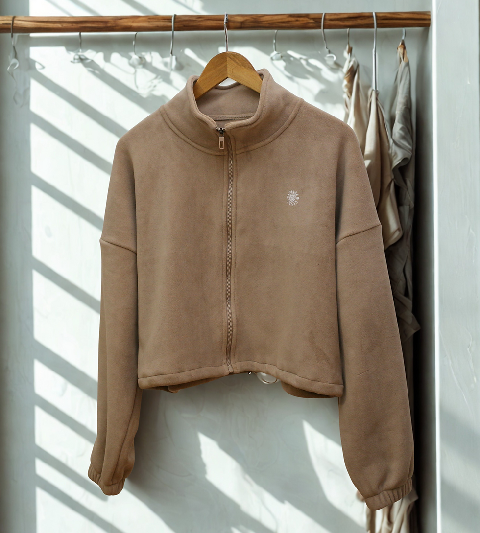 Brown zip-up jacket on a wooden hanger, with sunlight creating striped shadows on a white textured wall. Other clothes hang in the background.