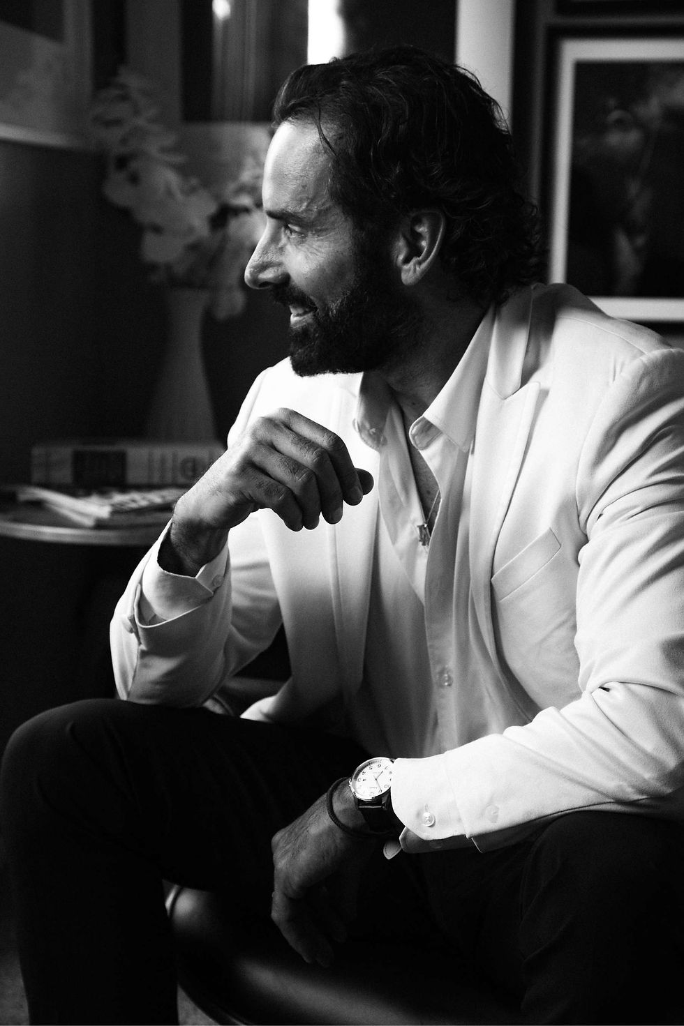 Black-and-white portrait of Christopher Gialanella in a white shirt, seated indoors in profile with hand raised. Photography: AM Reed