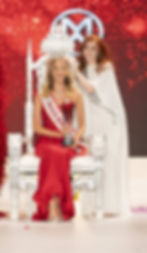 Grace Richardson in red gown and "Miss England" sash sits on ornate chair, holding trophy. Another woman places crown on her head. Red sparkly backdrop.