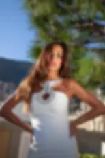 Sofia Valleri in a white dress with jeweled neckline poses outdoors. Pine tree and mountain in the background under a clear blue sky.