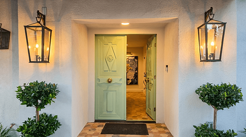 Sage green front door flanked by matching wrought iron lantern wall sconces on stucco entryway