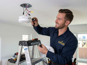 Licensed electrician installing a new 120V hardwired smoke detector on a ceiling in a Las Vegas home.