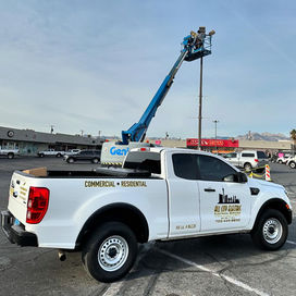 All City Electric commercial service truck in a retail parking lot with technicians operating a boom lift to repair high-reach pole lighting in Las Vegas.