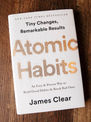 Atomic Habits by James Clear book cover on wood background
