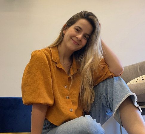 Laura, sentada no chão do seu consultório, em pose casual e descontraída, sorriso de canto