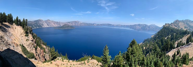 Panoramic view of a deep blue lake Tahoe surrounded by rugged cliffs and dense pine forests under a clear blue sky. Serene and majestic.