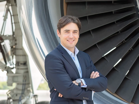 Jeremie Caillet steht vor einem Triebwerk eines grossen Flugzeugs und lächelt. Er trägt einen blauen Anzug, ein blaues Hemd und eine elegante Uhr.