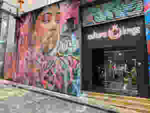 A photograph of street art outside a store called Culture Kings on Melbourne's Hosier Lane, a place famous for street art. Next to the storefront there is a mural of a woman that another graffiti artist has tagged over. (Credit: Pat Mitchell)