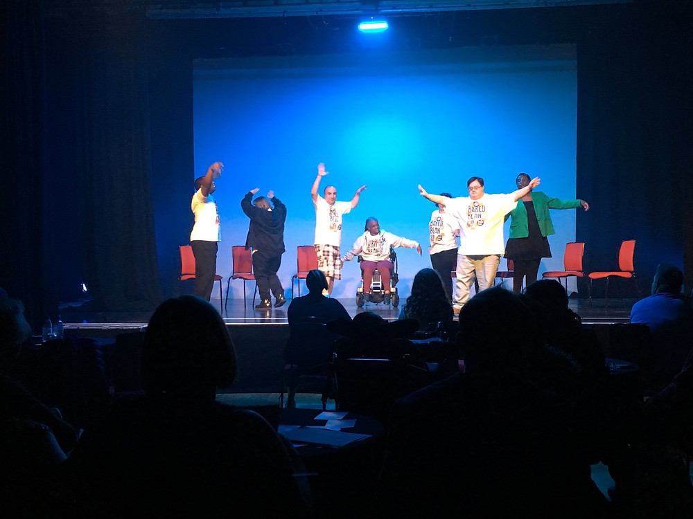 The Baked Bean Company onstage during their performance at the World Transformed in Brighton, September 2019. A group of actors with physical and learning disabilities raise their hands onstage during a play. (Photo: Baked Bean Company)