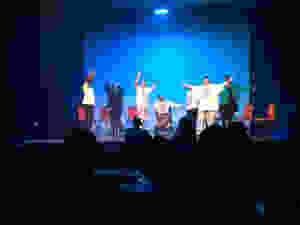 The Baked Bean Company onstage during their performance at the World Transformed in Brighton, September 2019. A group of actors with physical and learning disabilities raise their hands onstage during a play. (Photo: Baked Bean Company)