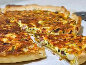 Quiche dorée avec garniture d'herbes aromatique, lard fumé et fromage. Une part manquante. Fond blanc, ambiance chaleureuse.