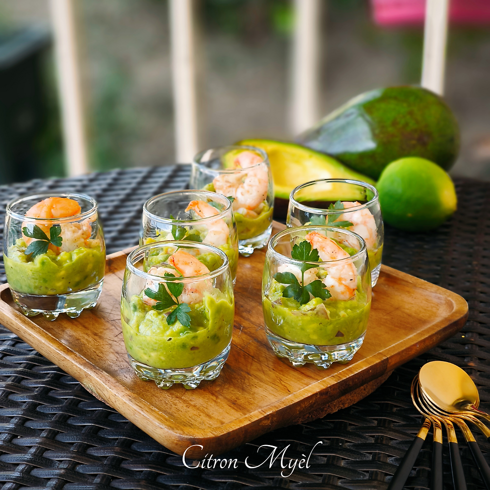 Six verrines de crevettes guacamole et persil frais sur une assiete en bois avec avocat et citron en arrière plan, le tout sur une table noir tressée