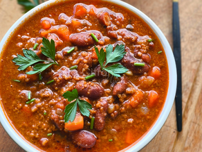 Chili con carne avec des feuilles de persil au-dessus dans un bol blanc sur une planche en bois