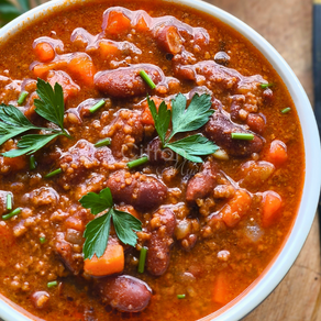 Chili con carne avec des feuilles de persil au-dessus dans un bol blanc sur une planche en bois